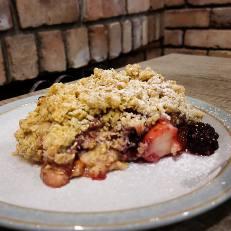 Slice of crumble dessert with berries on a plate against a brick wall background