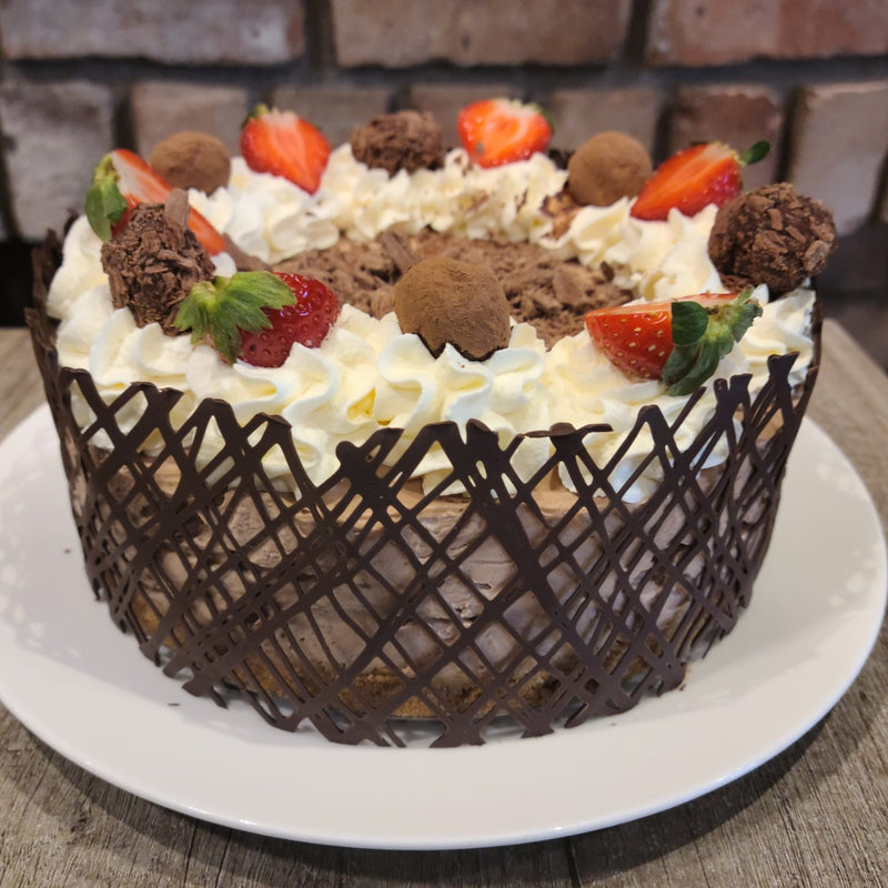 Cheesecake with whipped cream, strawberries, and chocolate truffles on a white plate.