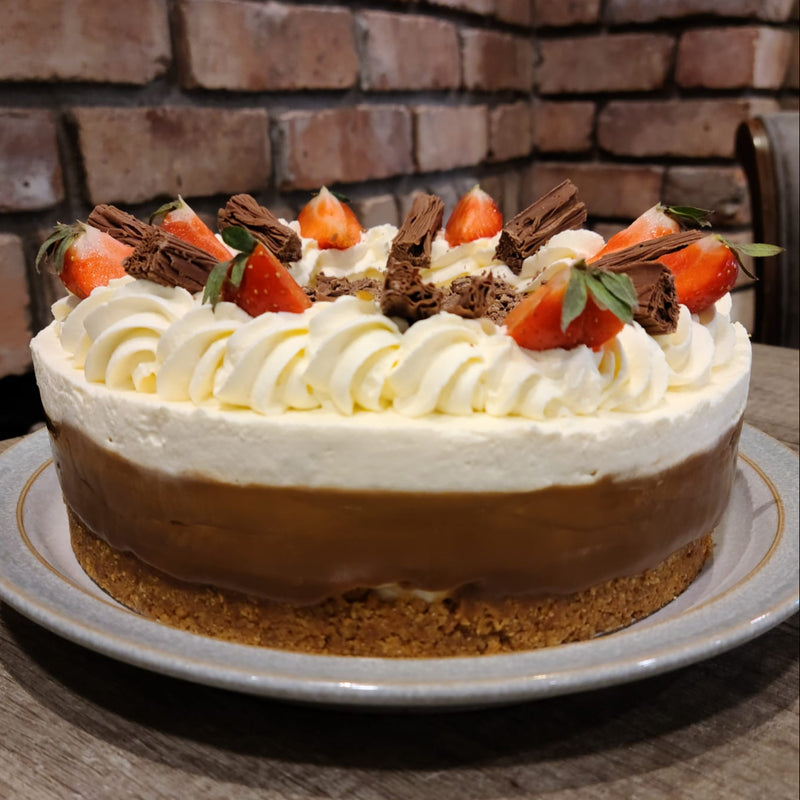 Banoffee with whipped cream and strawberries on a wooden table with a brick wall background