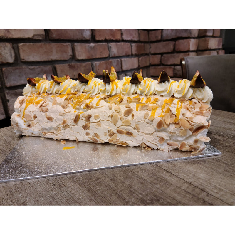 Roulade with almond flakes and passionfruit on a cake board against a brick wall.