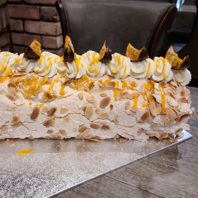 Roulade with almonds and passionfruit drizzle on a cake board.