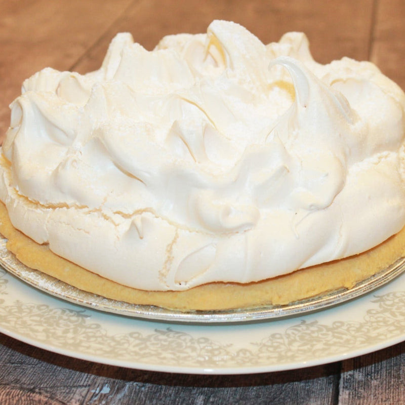 A lemon meringue pie topped with white meringue on a plate with a decorative edge.